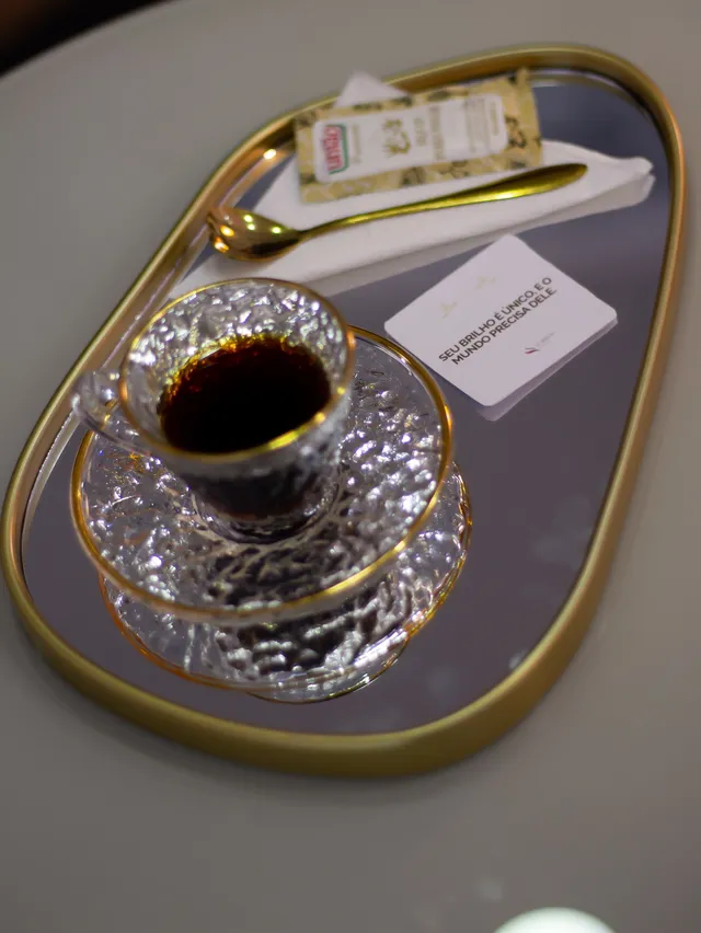 Café servido em xícara de vidro sobre bandeja dourada